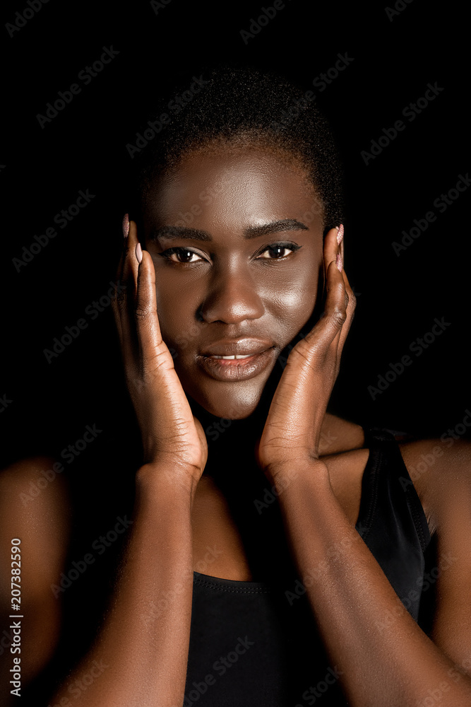 portrait of beautiful african american woman touching face with hands and smiling at camera isolated on black portrait of beautiful african american woman touching face with hands and smiling at camera isolated on black