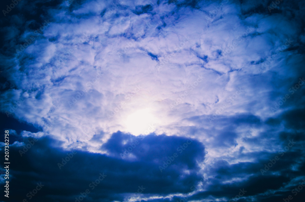 The sun is surrounded by gray and dark blue clouds