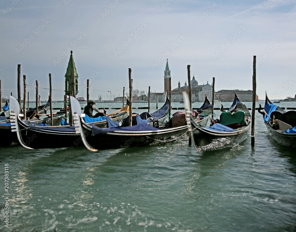 Many gondolas parked in the Venetian lagoon photographed with th