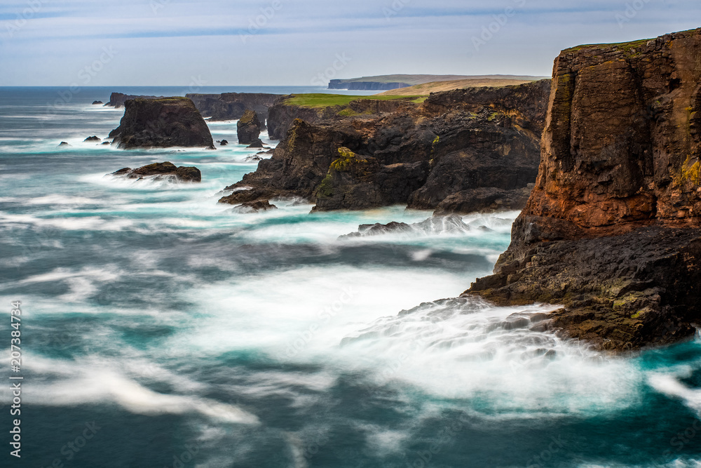 The wild Atlantic Ocean crashes against the sea stacks, rocks, and cliffs along the Western shore of Shetland Islands at Eshaness