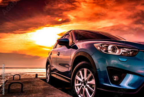 Blue compact SUV car with sport, modern, and luxury design parked on concrete road by the sea at sunset. Front view of beautiful hybrid car. Driving with confidence. Travel on vacation at the beach. © Artinun
