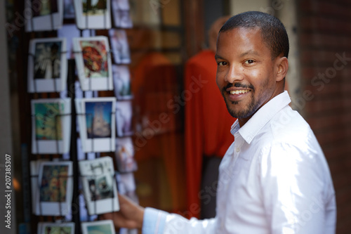 Handsome young African man in white shirt looking at camera and chooses postcard