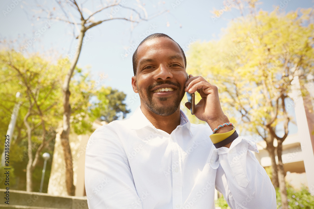 Young handsome african man talking on smartphone while sitting at sunny city park Young handsome african man talking on smartphone while sitting at sunny city park
