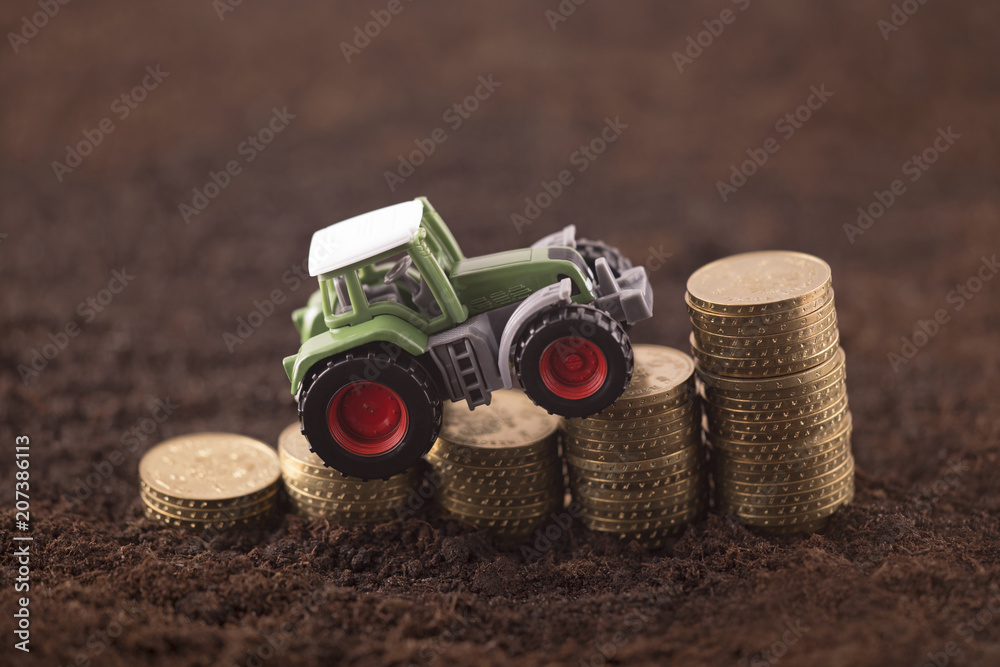 Obraz premium Tractor miniature with coins on fertile soil land