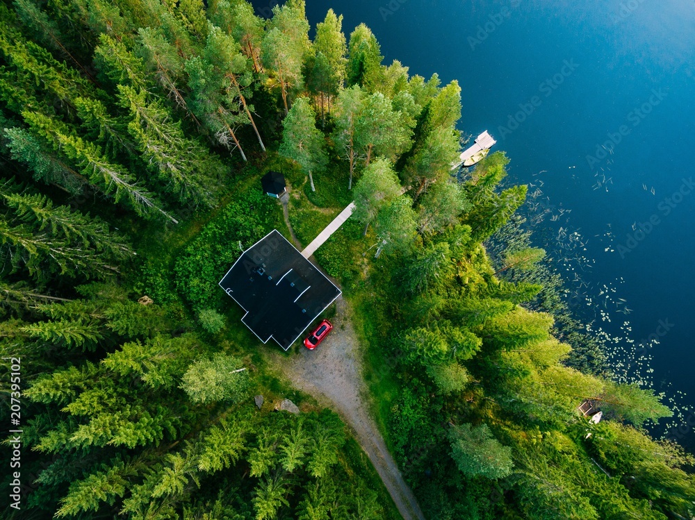 Naklejka premium Aerial view of wooden cottage in green forest by the blue lake in rural summer Finland