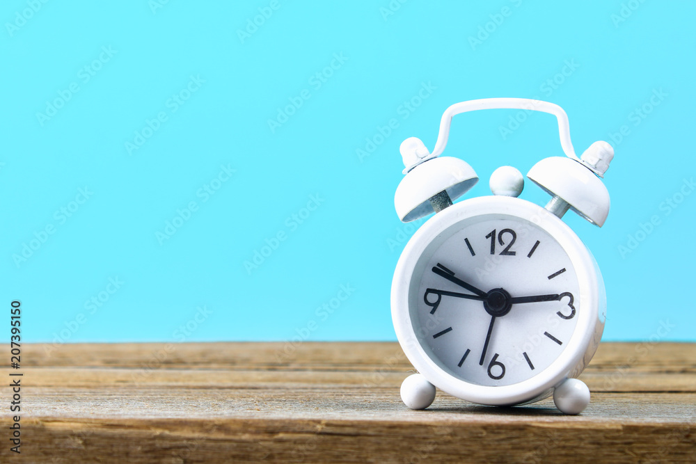 White small alarm clock on a wooden shelf on a blue pastel background. Minimalism White small alarm clock on a wooden shelf on a blue pastel background. Minimalism