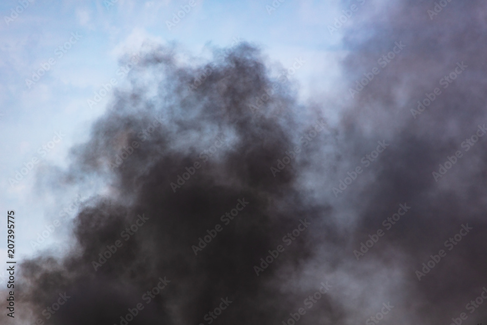 Black smoke against a blue sky with clouds Black smoke against a blue sky with clouds