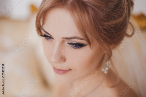 Gorgeous beauty young bride portrait. Beautiful bride with wedding makeup and jewelry wreath on long curly hair. Bridal fashion model with blue eyes posing in interior.