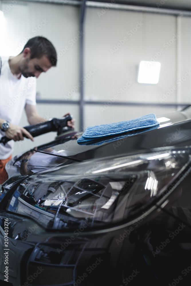 Car detailing - Hands with orbital polisher in auto repair shop. Selective focus.