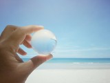 Hand holding glass global with blue sky and sea background