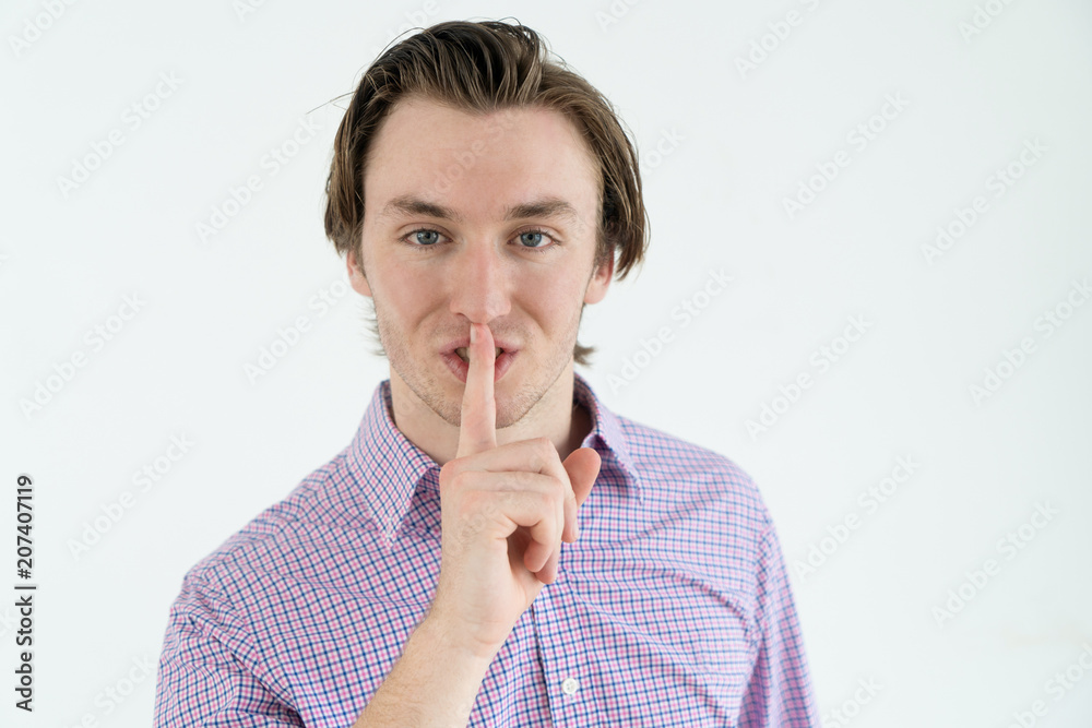 Confident handsome young man in casual shirt making silence sign and looking at camera. Content calm male entrepreneur having secret. Hush concept Confident handsome young man in casual shirt making silence sign and looking at camera. Content calm male entrepreneur having secret. Hush concept