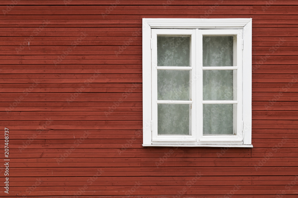 White window covered with lace curtains on red wooden wall, in Estonia.