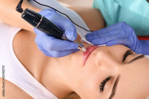 Cosmetologist making permanent makeup on woman s lips