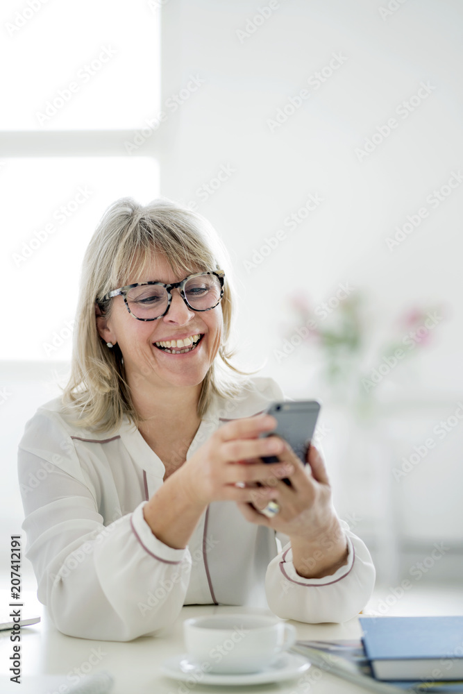 Laughing mature businesswoman looking at cell phone at desk Laughing mature businesswoman looking at cell phone at desk