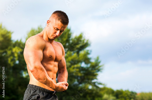 Young bodybuilder flexing muscles outdoors