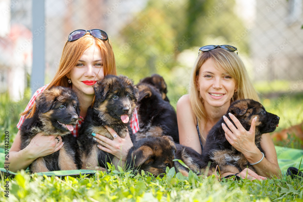 Two young smiling women lying on grass with small puppies of german shepherd Two young smiling women lying on grass with small puppies of german shepherd