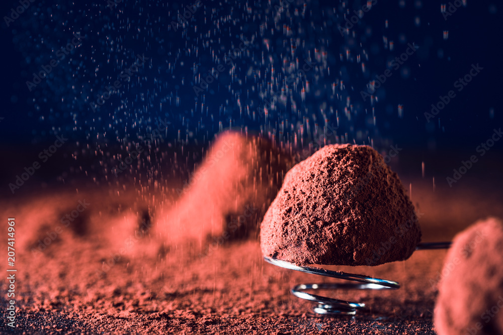 Chocolate truffles and falling cocoa powder on blue background, macro