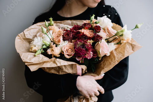Jonge bloemist vrouw knuffelen vers gemaakte bloeiende bloemboeket van rozen, eustoma, chrysanten in bruine kleuren op de grijze muur achtergrond.