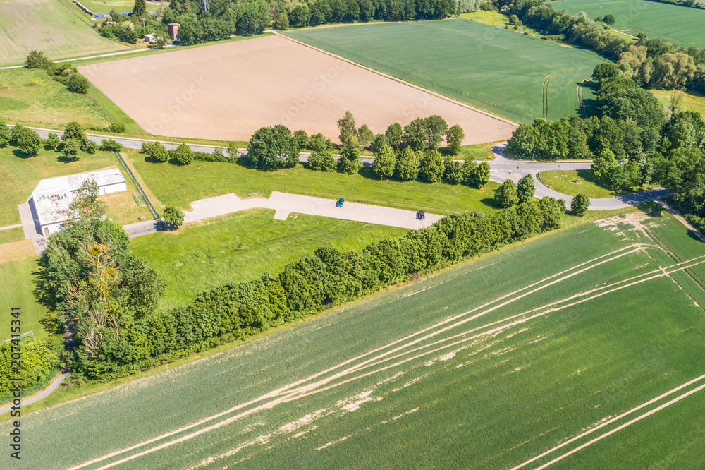 Aerial view of a small parking lot wiping rows of bushes and trees in front of the edge of an arable land
