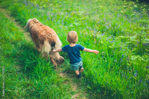 Little boy running in meadow with dog