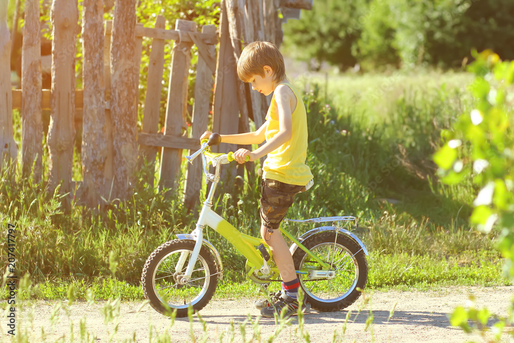 Sunlit profile portrait of six year old boy learning to ride a bicycle in the village