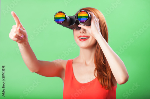 Redhead girl with binocular and gay flag on blue background.