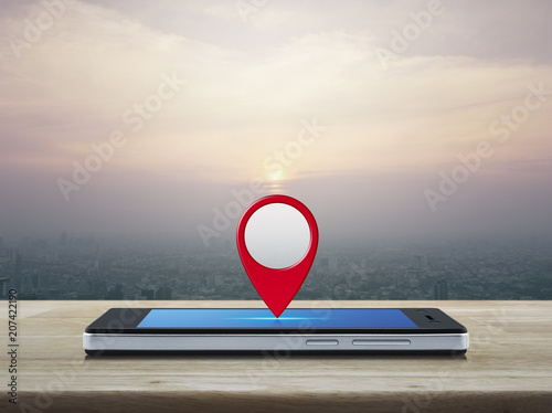 Map pin location button on modern smart phone screen on wooden table over city tower at sunset, vintage style, Map pointer navigation concept