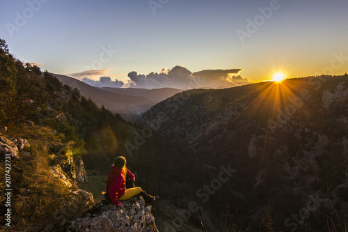 girl sitting on a cliff in mountains at sunset