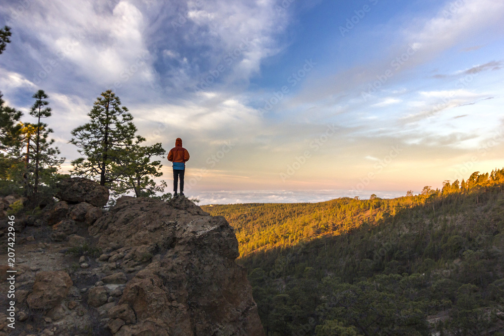 Obraz premium man standing on rock at sunrise with forest below