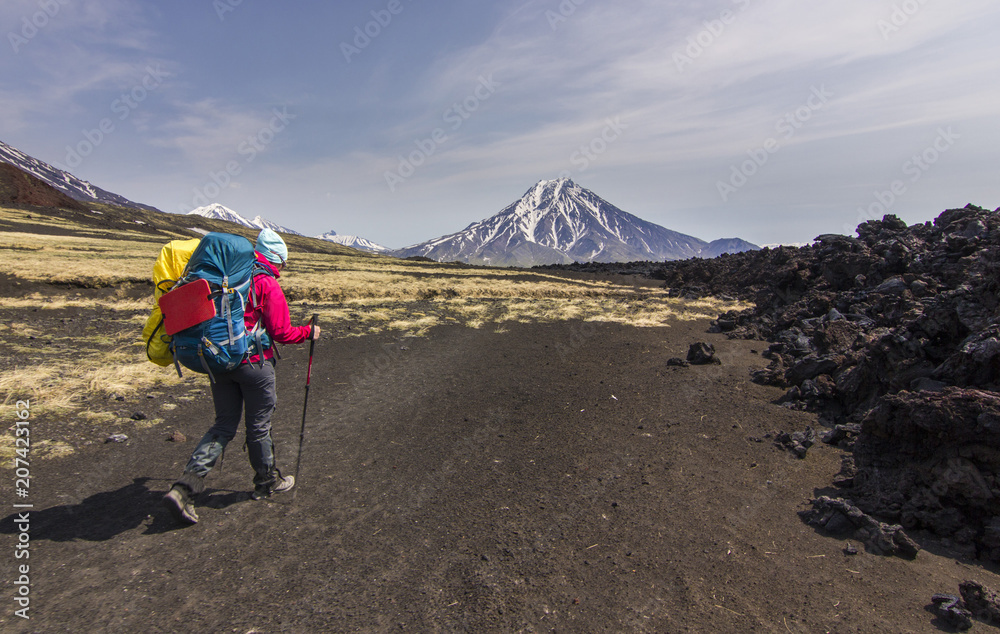 tourist going on volcanic slag with view on snowy volcanoes