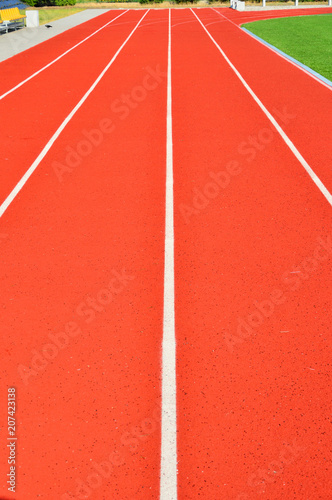 Czerwona tartanowa bieżnia i białe pasy rozdzielające tory dla biegaczy.