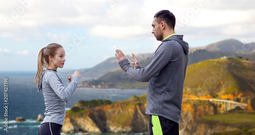 fitness, sport, martial arts and people concept - happy woman with personal trainer working on strike over bixby creek bridge on big sur coast of california background photo
