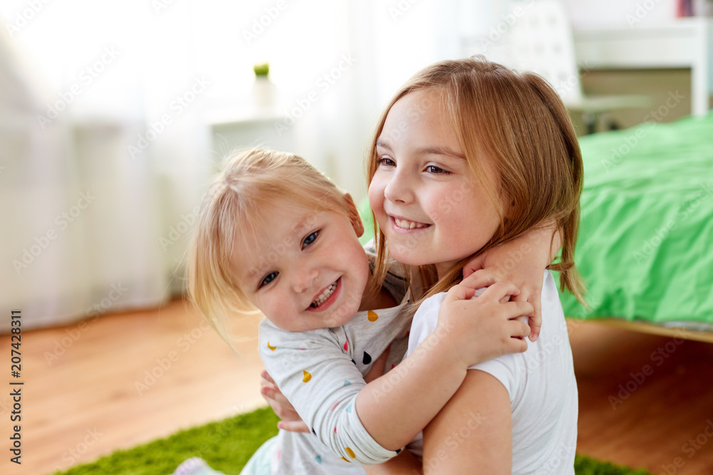 childhood, family, expressions and people concept - happy little girls or sisters hugging at home