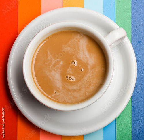 Cup of coffee with milk or cappuccino beverage on colorful as rainbow background. Drink with caffeine or cocoa with milk. Coffee on colorful positive background, top view. Dose of energy concept