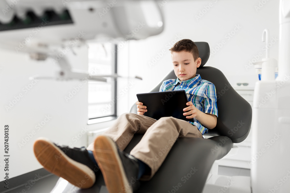 medicine, dentistry and technology concept - happy kid patient with tablet pc computer at dental clinic