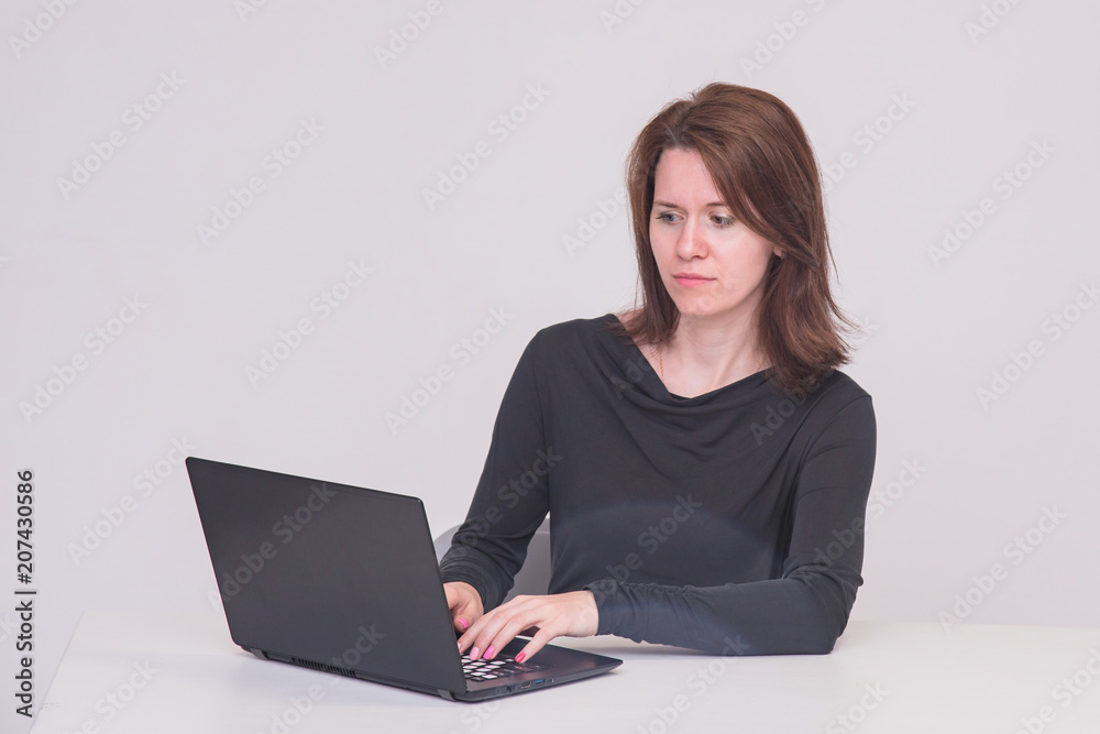 Portrait of beautiful brunette manager girl on white background sitting at table behind laptop Portrait of beautiful brunette manager girl on white background sitting at table behind laptop