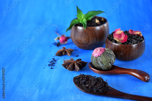 Blossom, black and green sorts of tea in wooden cups and spoons and two anise stars against the blue background