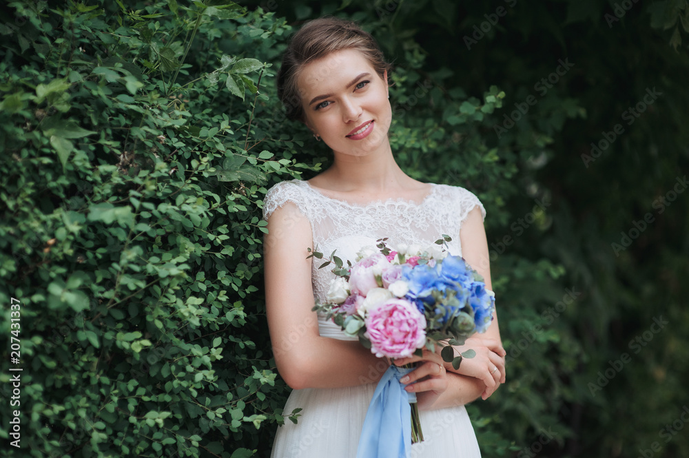 A beautiful and young bride in a lace dress is standing in nature and holding a bouquet in green foliage, in nature. Portrait of a gentle bride with a bouquet. A beautiful and young bride in a lace dress is standing in nature and holding a bouquet in green foliage, in nature. Portrait of a gentle bride with a bouquet.