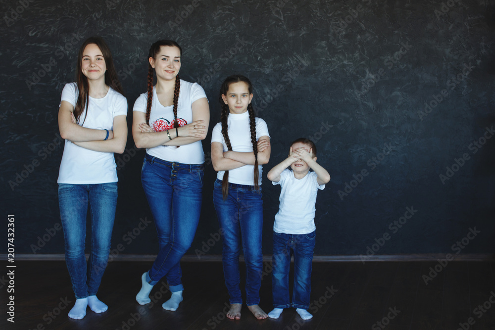 Three sisters with long braids and their brother in blue jeans and white  T-shirts stand in the studio with dark blue walls. Stock Photo | Adobe Stock