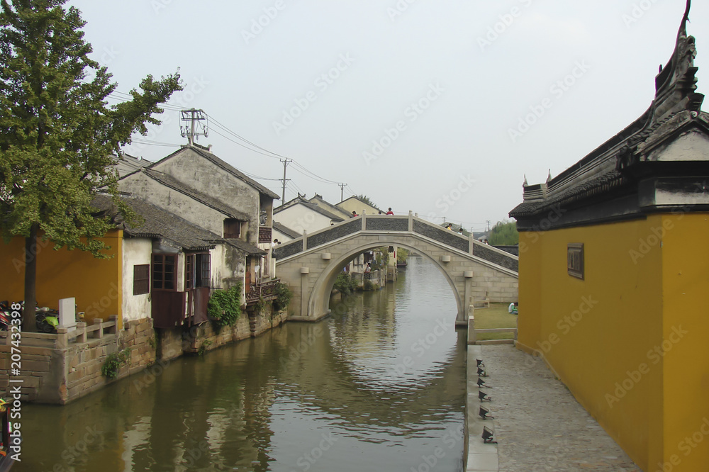 ancient Suzhou (China): arch stone bridge across the canal, compact street with old houses facing right the water