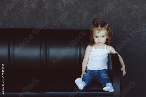 Little blonde girl sitting on black couch