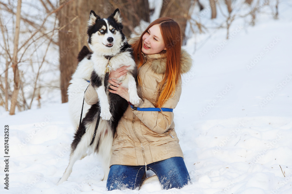 A girl with long red hair plays with a Yakut husky in a snow park. A girl with long red hair plays with a Yakut husky in a snow park.
