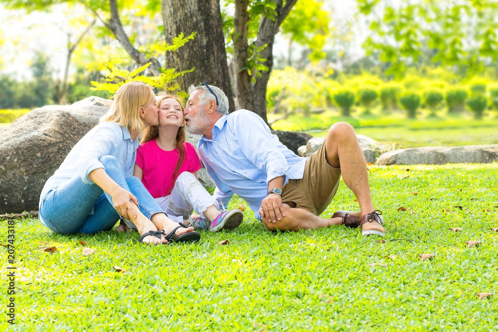 Grandfather and grandmother of the elder family relaxing and kissing granddaughter on the grass in the park. Grandfather and grandmother of the elder family relaxing and kissing granddaughter on the grass in the park.