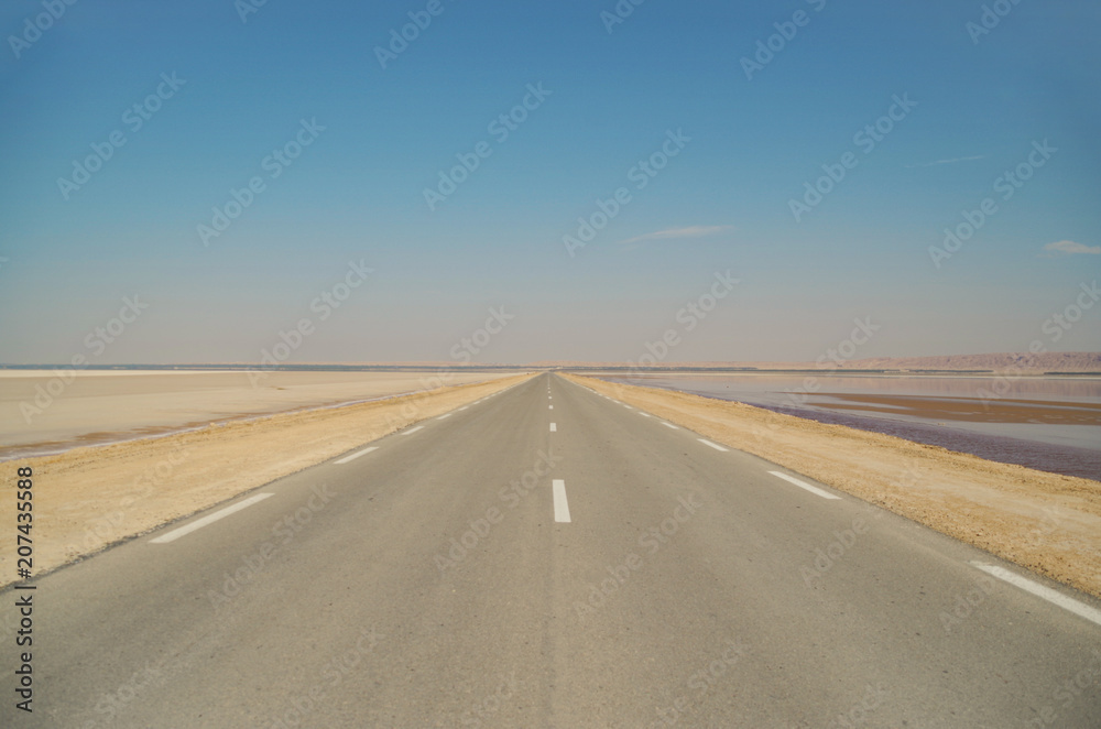 Road on a crest of the constructed dam. Large salt lake Chott el Djerid. Largest salt pan of the Sahara Desert. Below sea level. Nature and travel. Tunisia