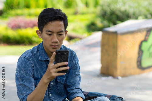Asian young man using mobile phone at park