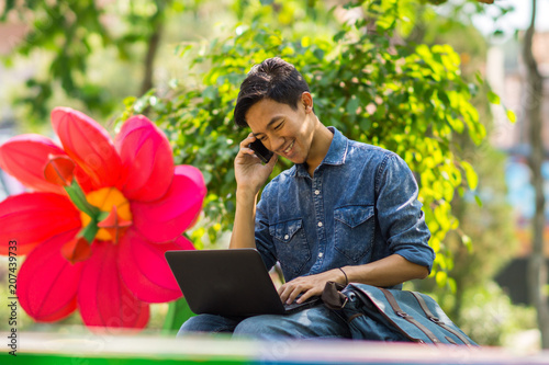 Asian young man with a laptop and smartphone sitting outdoor in a park