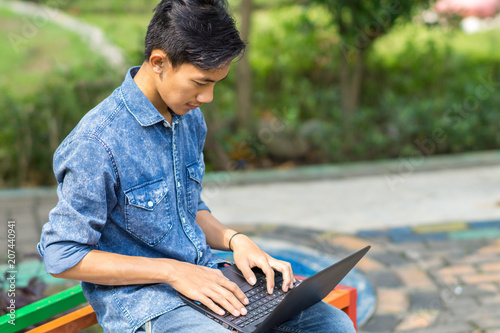 Asian young man using laptop outdoor.