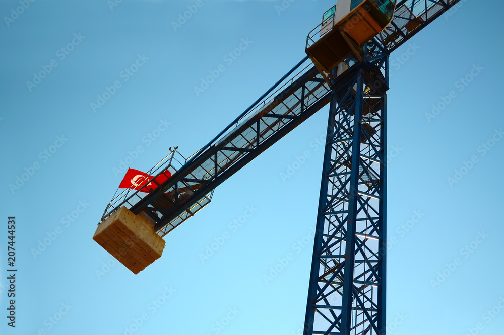 Construction crane with the Turkish flag on top on the cloudless sky, view from the bottom up Construction crane with the Turkish flag on top on the cloudless sky, view from the bottom up