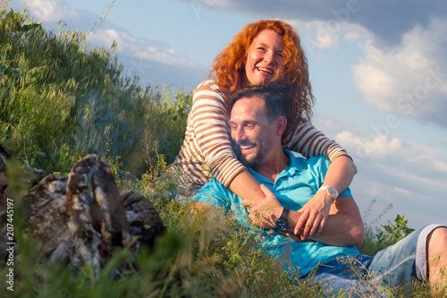 Happy loving smile attractive couple laying by bonfire hugging in grass and clouds. Couple loves casual watches