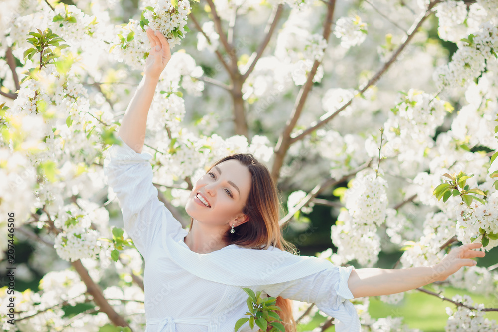 Young beautiful blonde woman in blooming almonds garden.